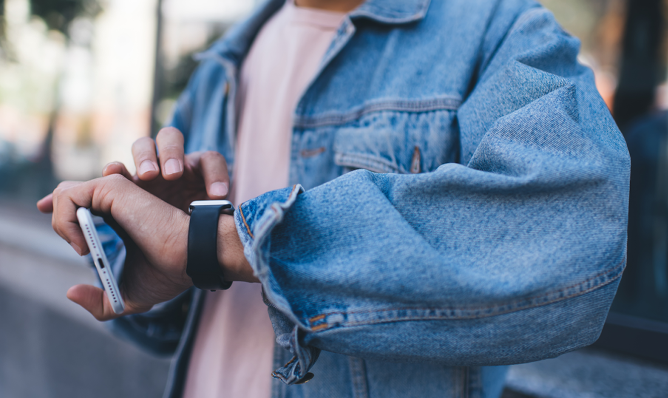 man kijkt en scrolt op zijn smartwatch en houdt in zijn andere hand zijn telefoon