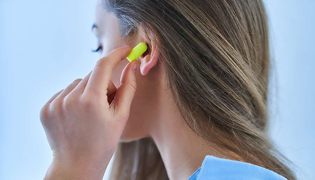 Vrouw doet felgele oordopen in haar oor om gehoorbeschadiging te voorkomen bij festival.