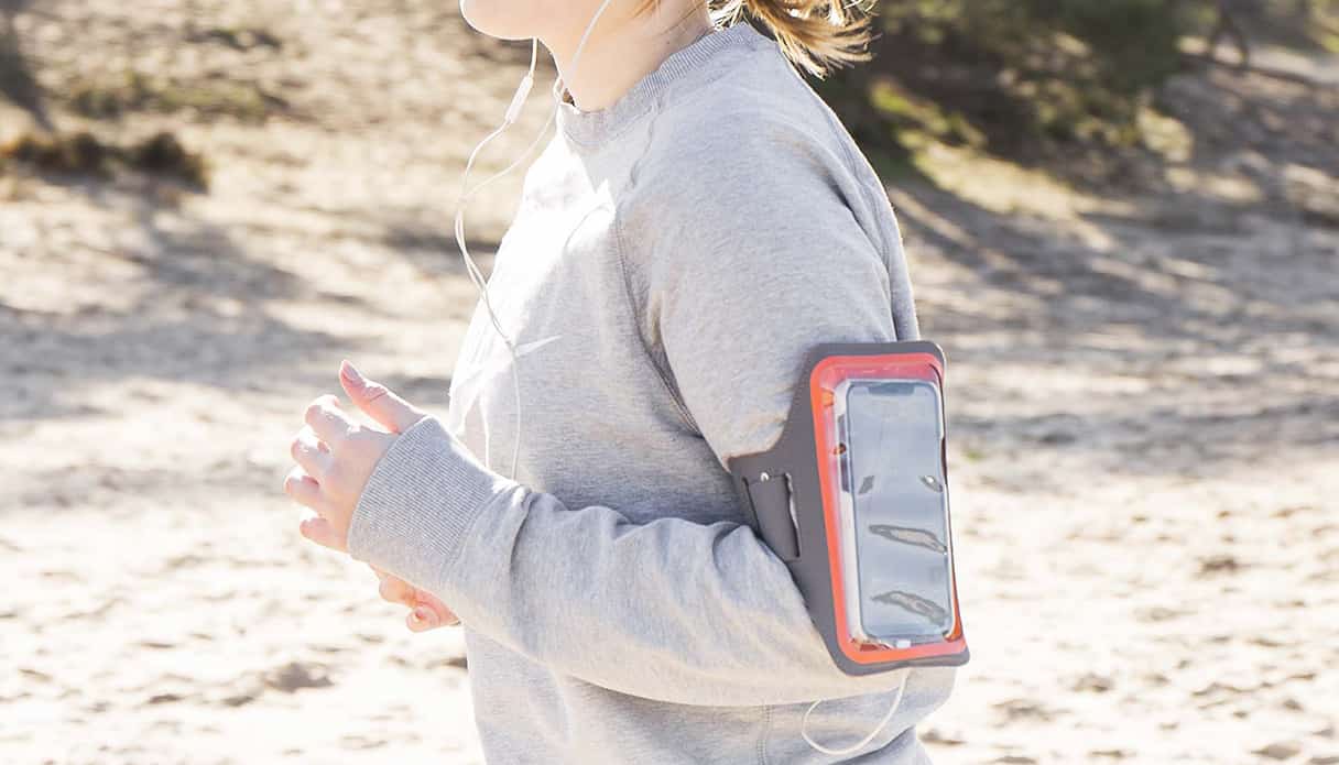 Vrouw is aan het hardlopen op de heide en draagt een hardloop armband waar ze haar telefoon in kan opbergen.