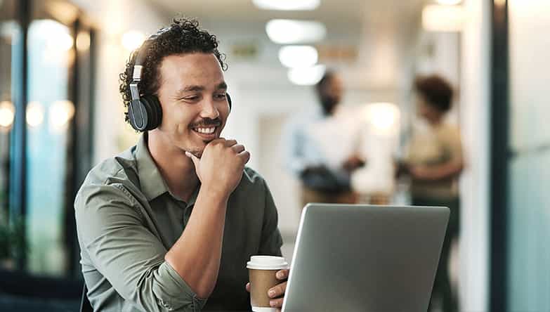 Man werkt in een kantoortuin en heeft geen last van omgevingsgeluiden dankzij de noise cancelling in zijn koptelefoon.