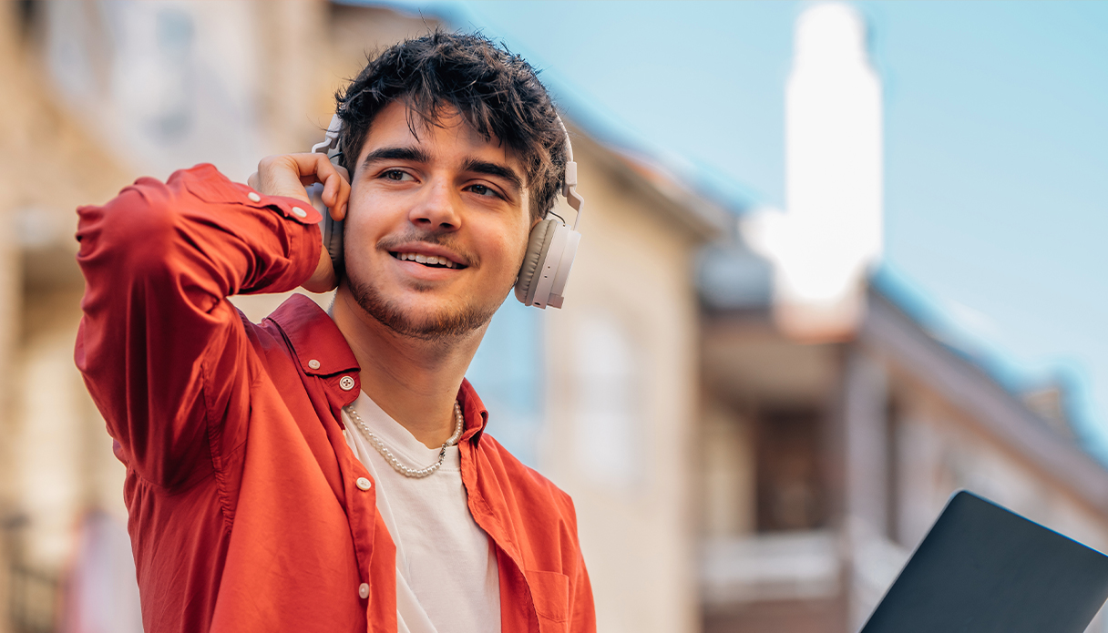 Man met rode blouse zit buiten naar muziek te luisteren via zijn noise cancelling koptelefoon.