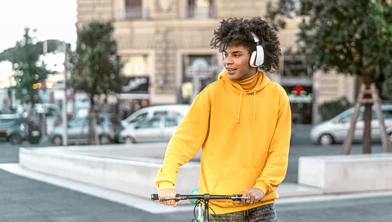 Man is onderweg met de fiets in zijn hand en luistert naar muziek via zijn draadloze koptelefoon.