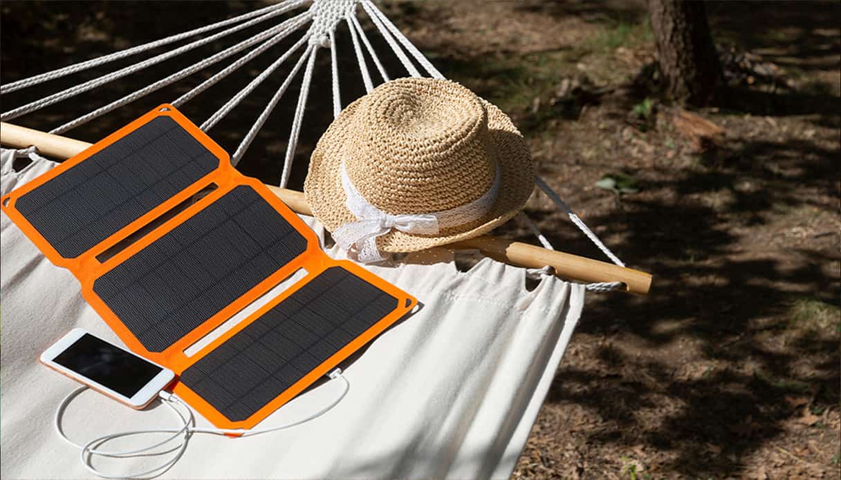 Een solar powerbank ligt op een hangmat in de zon verbonden aan een telefoon.