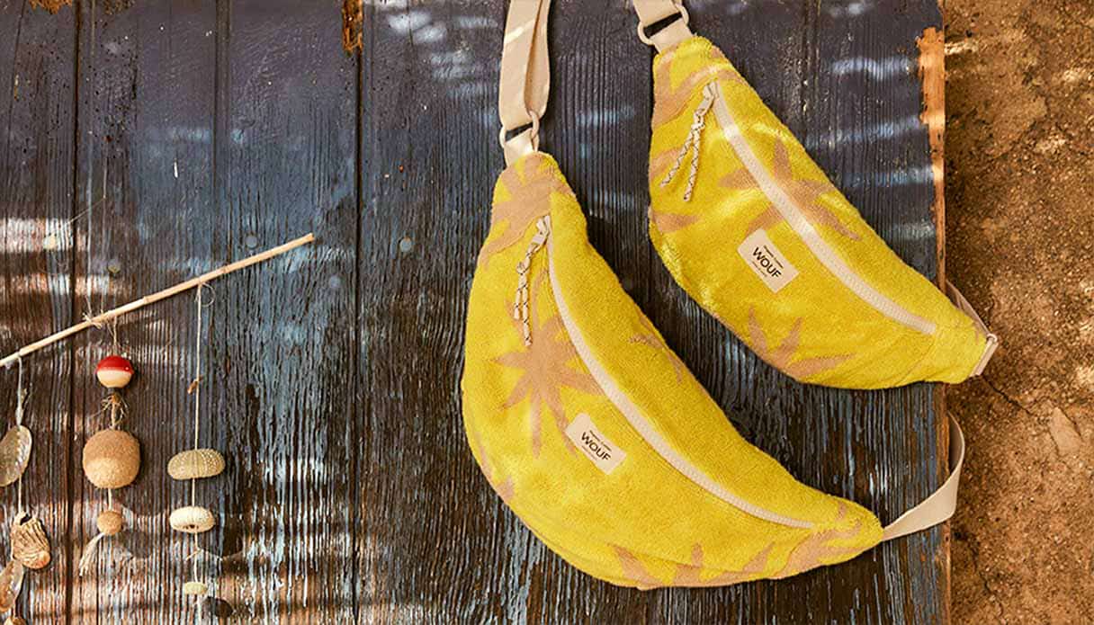 Twee gele Wouf waistbags hangen over een houten buitendeur heen.