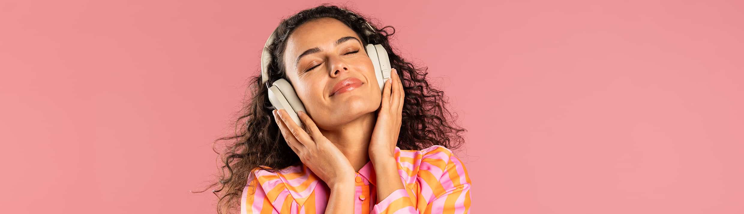 Op het strand staat een lachende vrouw met een felgele koptelefoon met noise cancelling op haar hoofd.