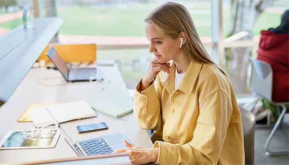 Vrouw zit te werken aan een bureau terwijl ze niet gestoord wordt door haar omgeving dankzij noise cancelling oordopjes.