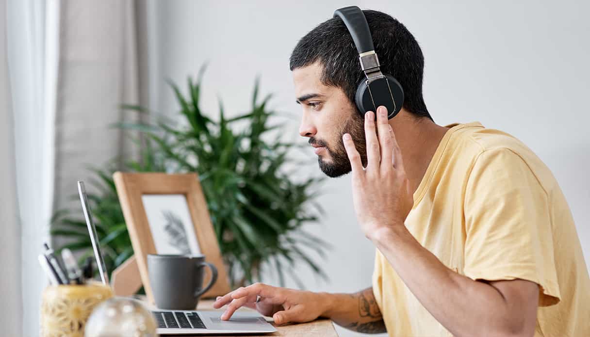 Man zit aan zijn bureau te kijken naar zijn laptop terwijl hij ook een koptelefoon met noise cancelling op heeft.