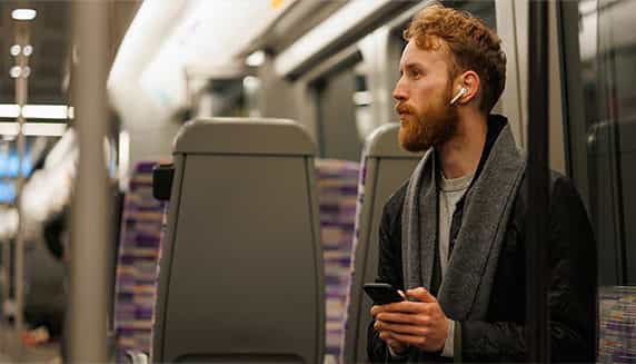 Man zit in de trein te luisteren naar zijn podcast via zijn oordopjes.