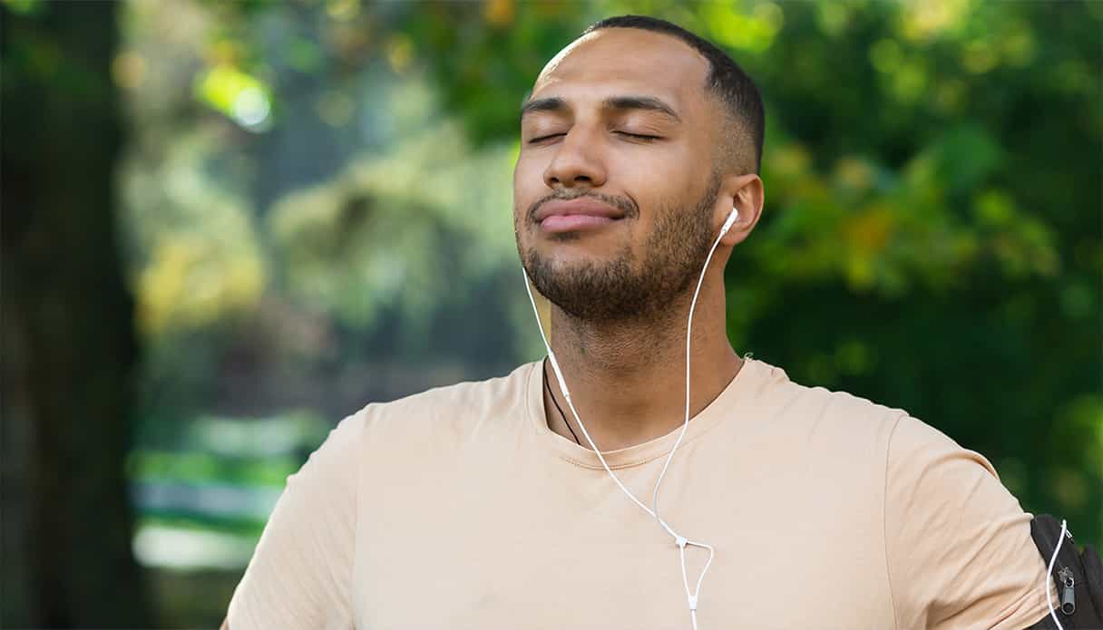 De man neemt een diepe adem terwijl hij in een park staat en naar zijn muziek luistert via zijn bedrade oortjes.