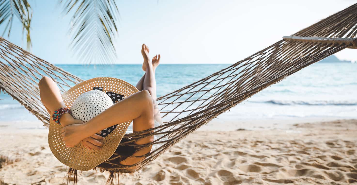 Vrouw met strandhoed is op vakantie en ligt in een hangmat op het strand, met uitzicht op de zee.