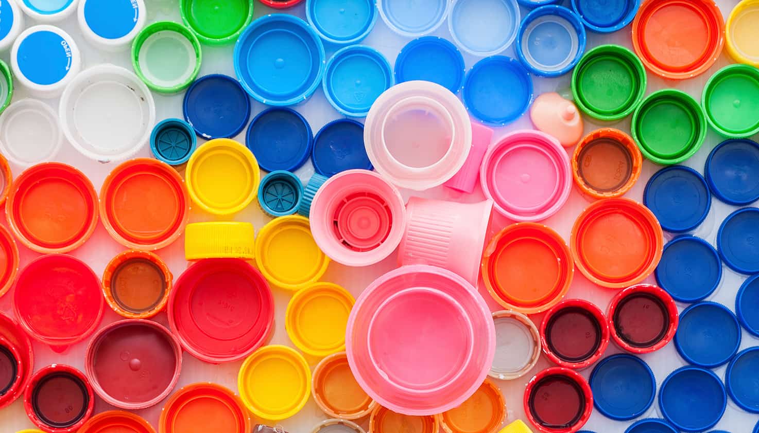 Een flatlay van een verzameling van plastic flessendoppen in verschillende kleuren.