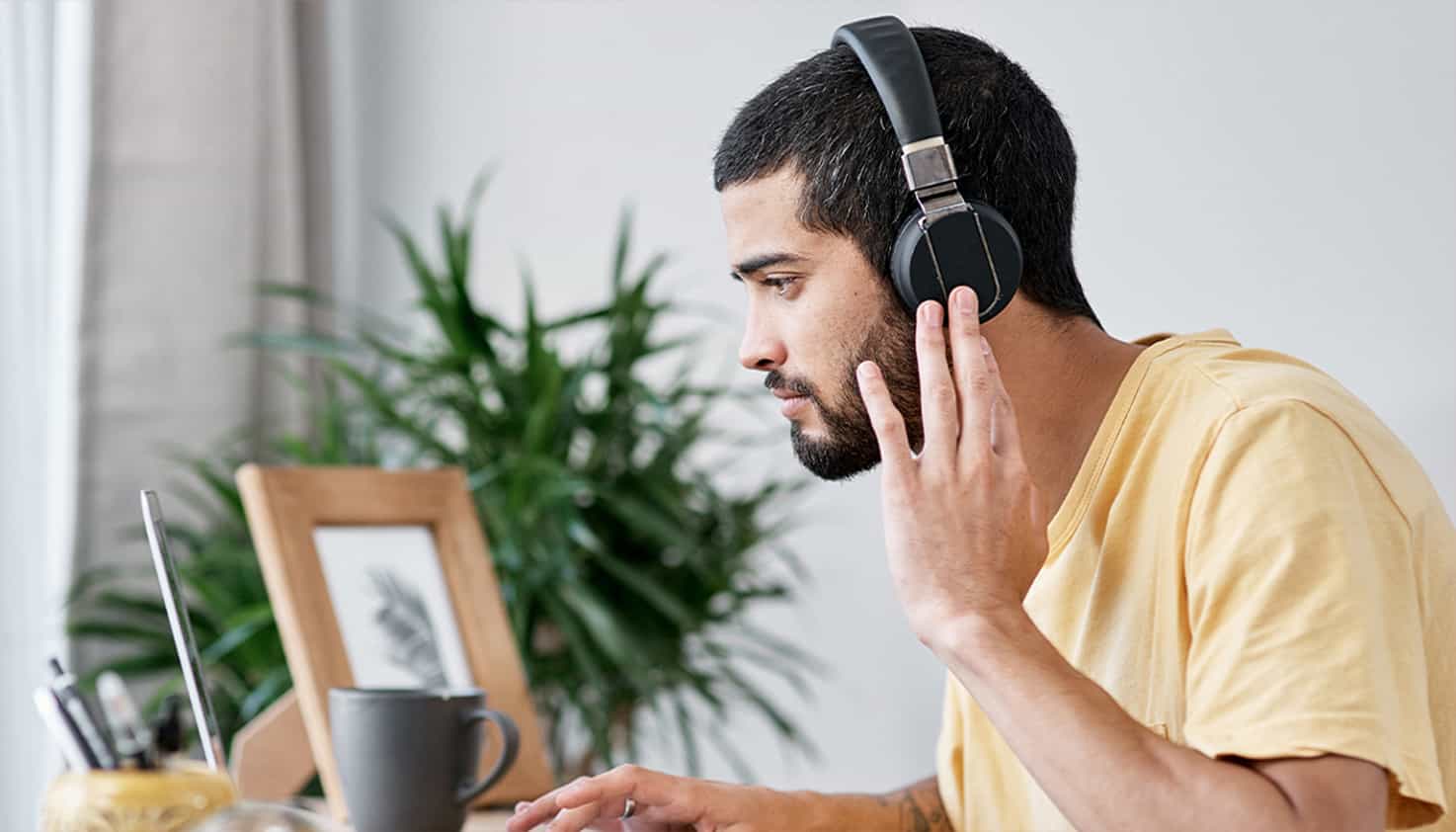 Man zit aan zijn bureau te kijken naar zijn laptop terwijl hij ook een koptelefoon met noise cancelling op heeft.