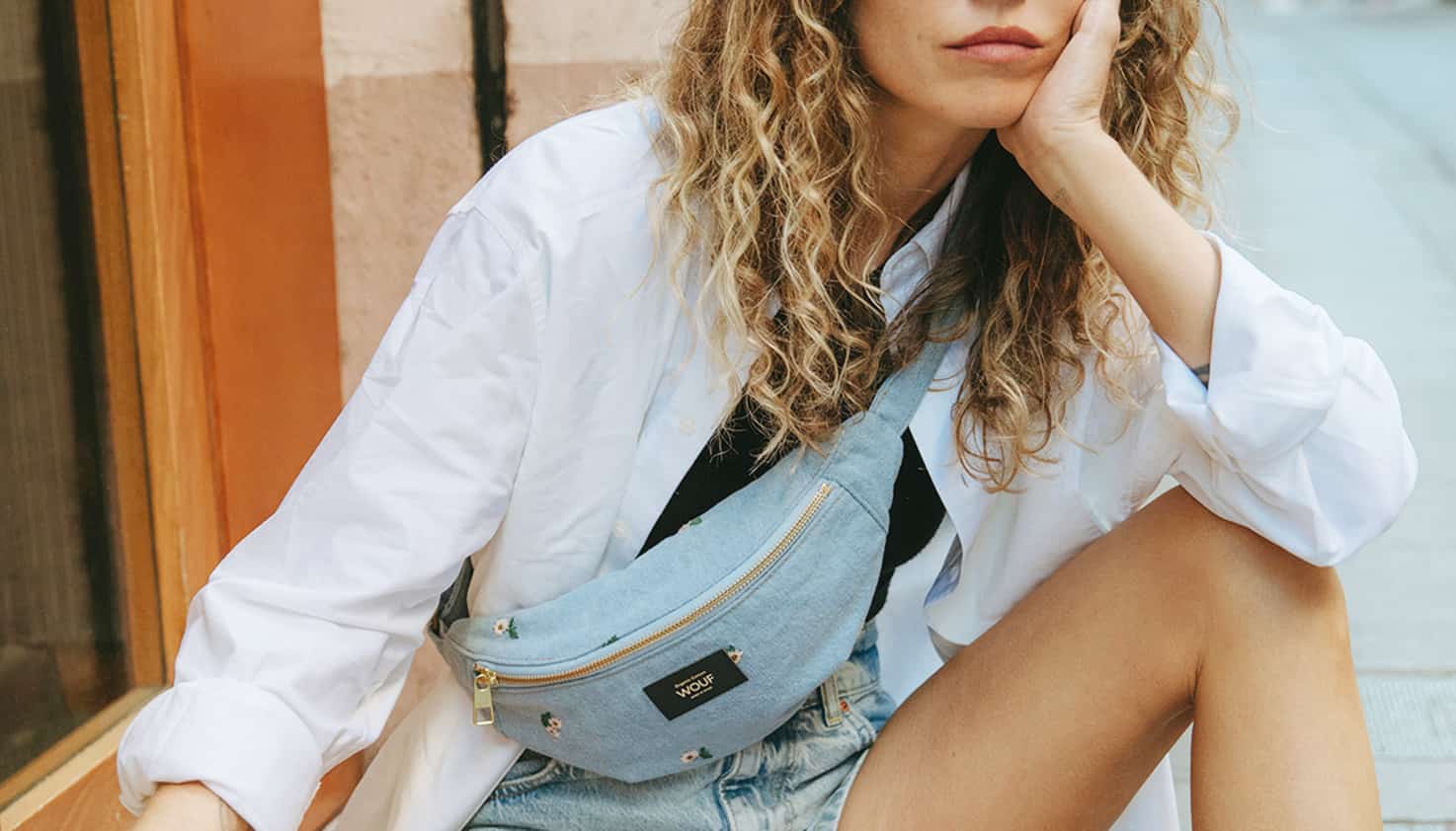 Vrouwelijk model zit op straat met een denim waistbag om haar schouder.