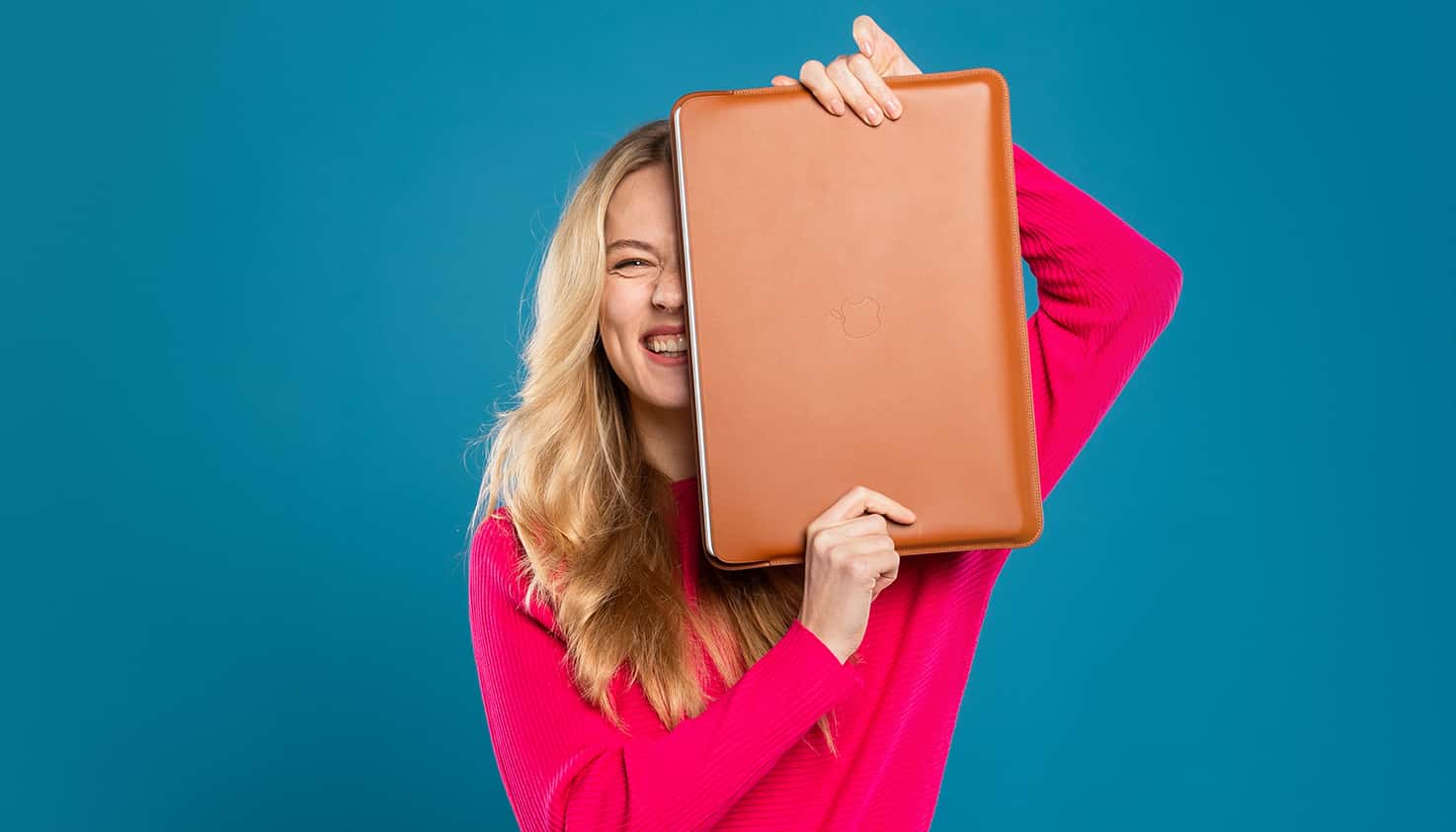 Vrouw staat centraal lachend met laptopsleeve of laptophoes voor zich, hierin zit een laptop die beschermt wordt.