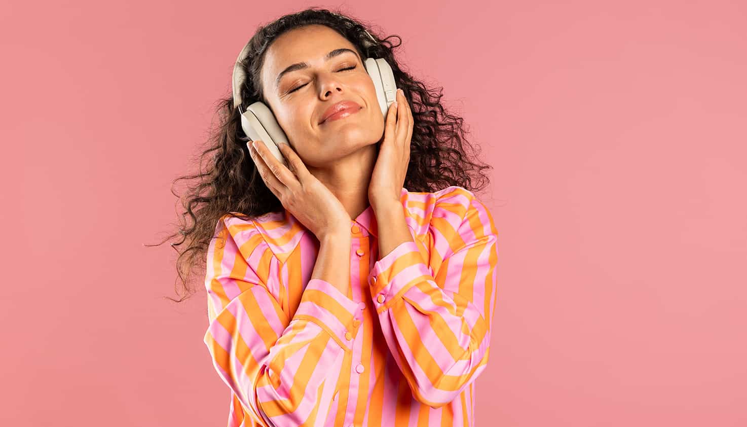 Op het strand staat een lachende vrouw met een felgele koptelefoon met noise cancelling op haar hoofd.