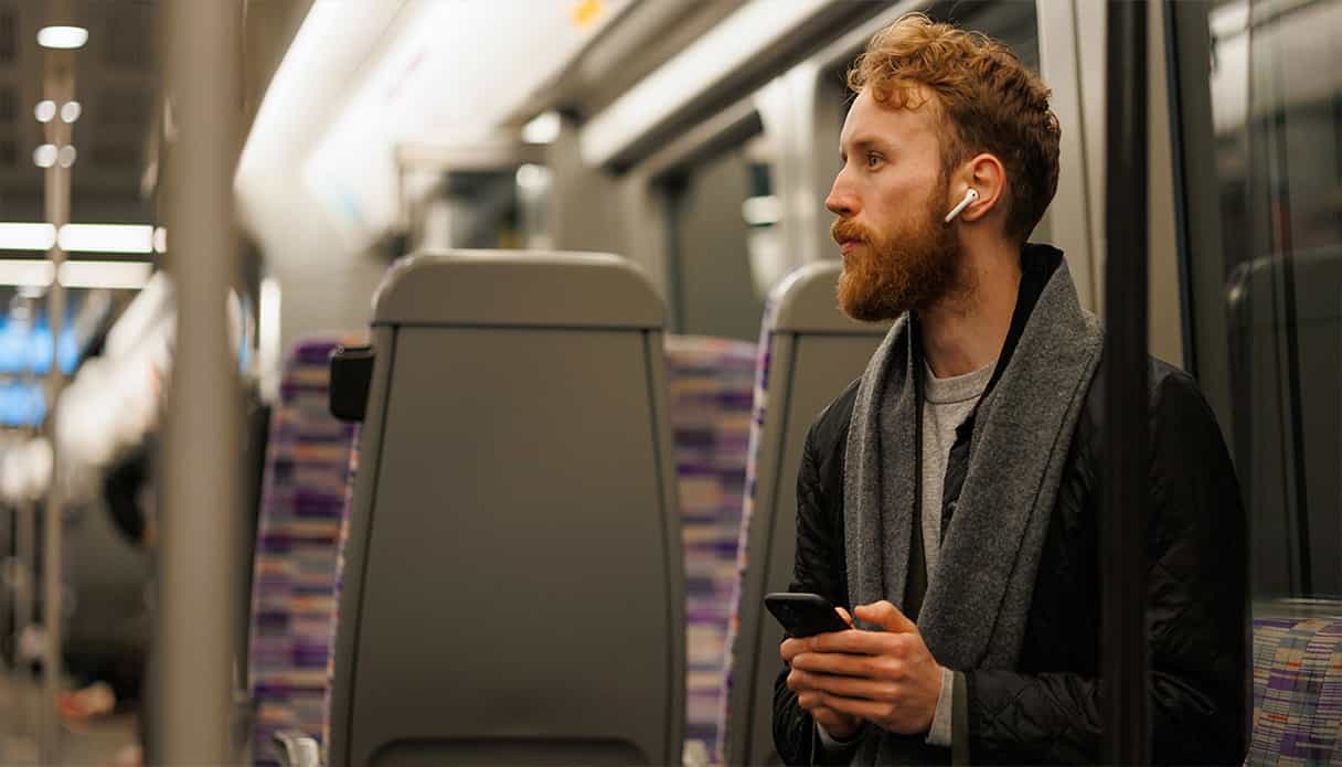 Man zit in de trein te luisteren naar zijn podcast via zijn oordopjes.