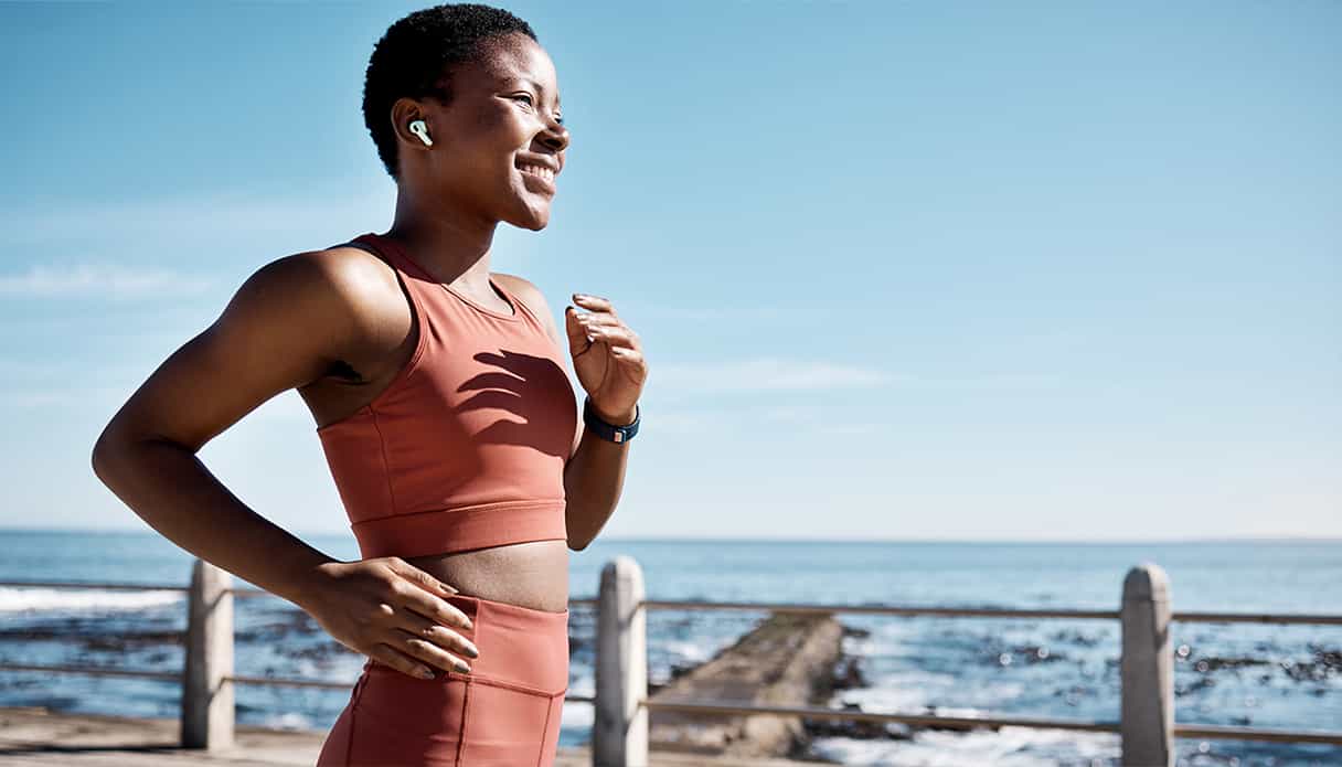 Vrouw is langs de kust aan het hardlopen en te genieten van haar muziek uit haar draadloze oordopjes.