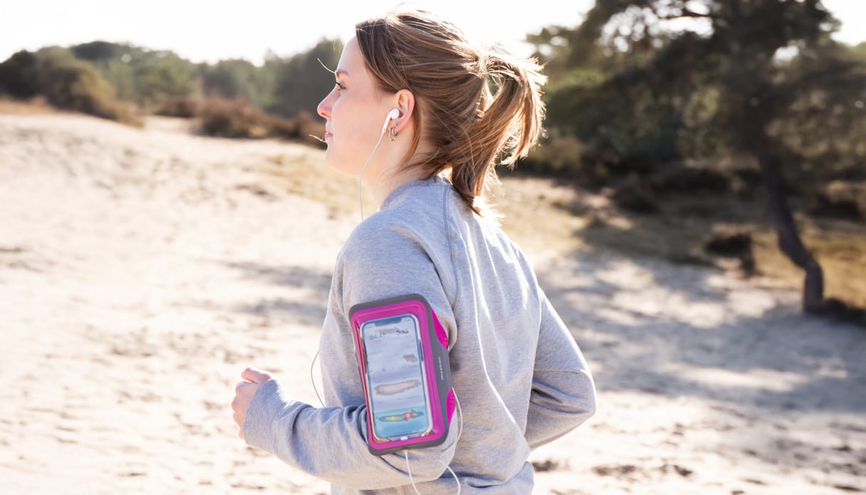 vrouw hardlopend in de duinen met een roze telefoonhouder om haar arm