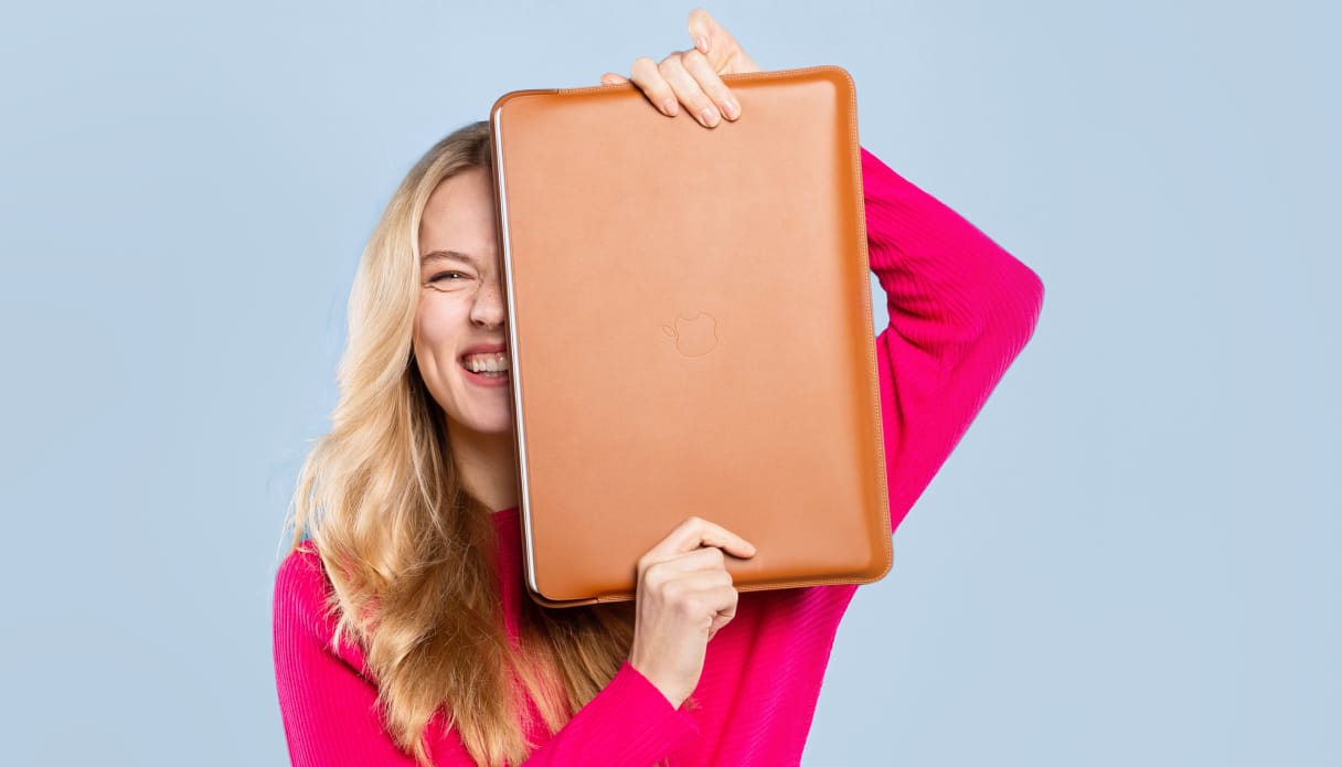 Een vrouw houdt een lederen cognac kleurige laptop hoes half voor haar gezicht