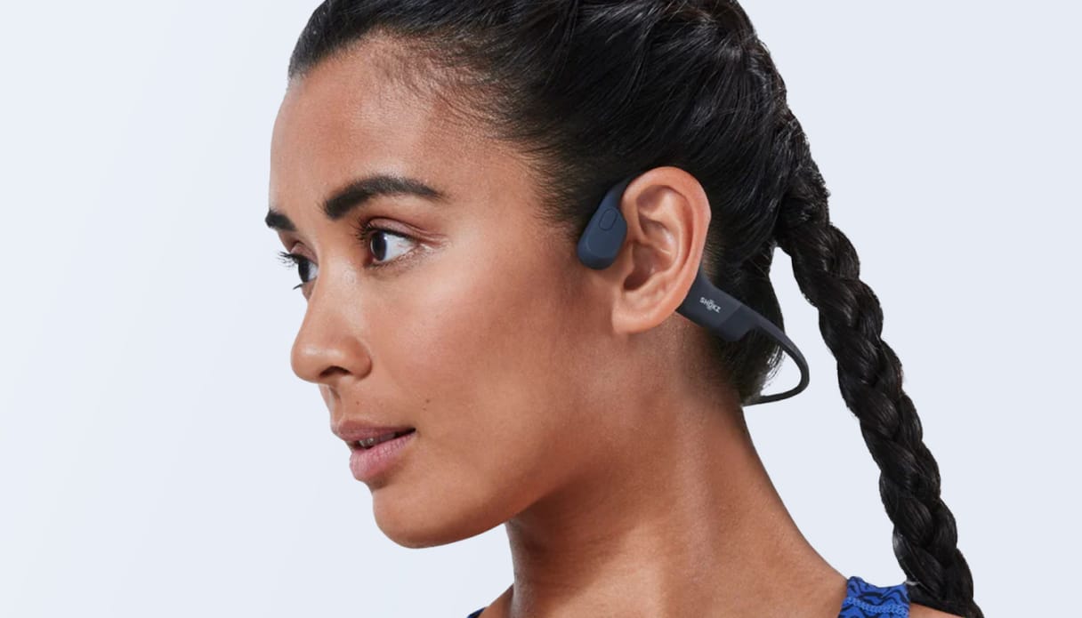 Een vrouw draagt de Shokz OpenRun Pro oordopjes met bone conduction in het blauw.