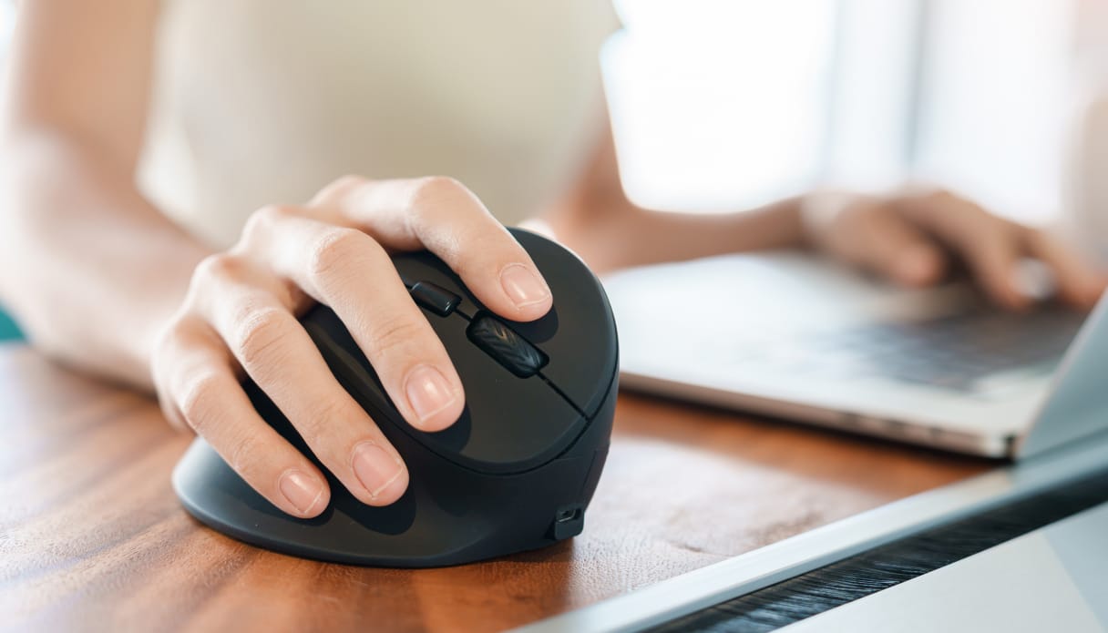 Een vrouw gebruikt de imoshion Ergonomische draadloze muis achter haar laptop.