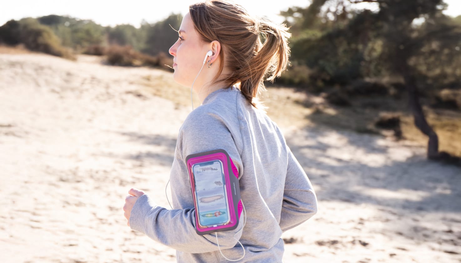 vrouw hardlopend in de duinen met een roze telefoonhouder om haar arm