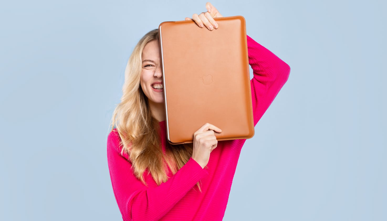 Een vrouw houdt een lederen cognac kleurige laptop hoes half voor haar gezicht