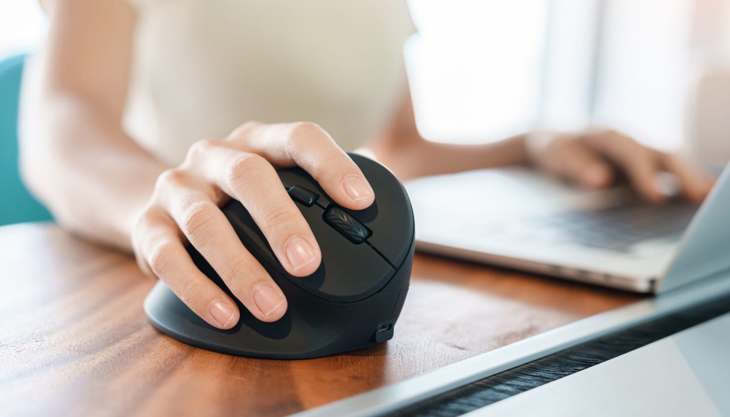 Een vrouw gebruikt de imoshion Ergonomische draadloze muis achter haar laptop.